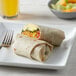 A plate with a burrito, tortilla chips, and a side of fruit next to a glass of orange juice.