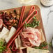 A board with Piller's Black Kassel Picante Salami Whips, cheese, and nuts on it.