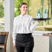 A woman in a black apron holding a tray with bottles and glasses on it.