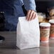 A hand holding a Bagcraft Packaging Dubl-Wax white paper bag over a wood surface.