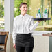 A woman in a black apron holding a tray with a bottle and glass on it.