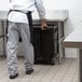 A man in a chef's uniform standing next to a black Choice mobile ice bin with wheels.