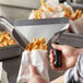 A person using a Prince Castle aluminum scoop to bag french fries.