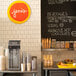 A Vitamix countertop milkshake machine on a counter in an ice cream shop with a blackboard sign above it.