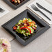 A black WNA Comet Milan Grand square plastic lunch plate with salad and a fork on a table.