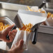 A person using a Prince Castle dual handle scoop to bag french fries.