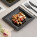 A black WNA Comet Milan Grand square plastic salad plate with food on a table.