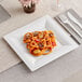 A WNA Comet white plastic dinner plate with spaghetti and meatballs on it on a table.