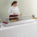 A woman in a white apron serving food from an Avantco countertop food warmer at a buffet.