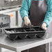 A person holding a black Cambro tray of utensils.