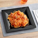 A WNA Comet black plastic square dinner plate with a plate of spaghetti and meatballs on it.