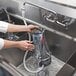 A person using a Vitamix Rinse-O-Matic to clean a blender container in a sink.