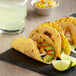 A group of Mission tortacos with meat, avocado, and vegetables on a black plate with a lime.