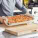 A person holding a Choice foil steam table pan of pasta with cheese and sauce.