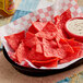 A basket of Mission red corn tortilla chips with a bowl of white sauce on a table.