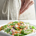 A hand pouring Regal Salad Seasoning on a salad.