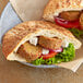 A sandwich with vegetables and meatballs on white pita bread.