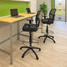 A black Boss drafting stool with a metal base and footring at a desk with a laptop.