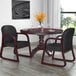 A Boss black fabric mahogany side chair next to a table with a glass and vase of yellow flowers.