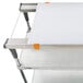 A white cutting board with orange handles on a metal shelf.