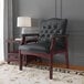 A black Boss Ivy League executive guest chair with mahogany legs next to a table with a white lamp on it.