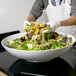 A person in gloves holding a American Metalcraft Mega Melamine bowl of salad.