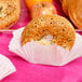 A white paper Hoffmaster fluted bagel cup holding a bagel on a table with apples.