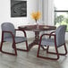 A mahogany-framed gray fabric Boss side chair next to a table with a glass and a plate on it.