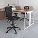 A black Boss drafting stool with adjustable arms at a desk with pencils and pens.