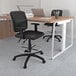 A black Boss drafting stool in an office with a desk and a computer.