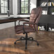 A Boss brown leather office chair at a desk with a laptop and bookshelf.