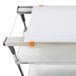 A white cutting board with orange handles on a metal shelf.