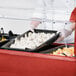 A person in a red uniform preparing food on a Carlisle portable salad bar.