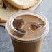 A plastic cup of coffee with ice cubes and a Fabri-Kal clear plastic strawless lid on a counter.