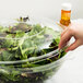 A hand putting a clear plastic dome lid on a bowl of salad.