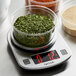 A Taylor digital kitchen scale with a bowl of green leaves.