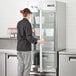 A woman opening an Avantco glass door reach-in refrigerator in a school kitchen.