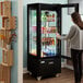 A woman standing in front of an Avantco refrigerated display case with drinks.