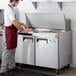 An apron-wearing man using an Avantco Mega Top Sandwich Prep Table to make a sandwich.