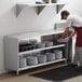 A man in a red apron standing in a professional kitchen putting plates in a Regency dish cabinet.