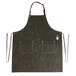 A Hardmill dark oak waxed canvas full length bib apron with brown leather straps on a counter in a professional kitchen.