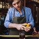 A man in a Hardmill dark oak waxed canvas full length bib apron peeling an orange.