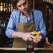 A man in a Hardmill Field Tan Waxed Canvas apron squeezing an orange over a drink.