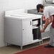 A man in a red apron putting a metal can into an enclosed stainless steel cabinet.