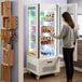 A woman standing in front of a white Avantco refrigerated display case.