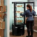 A woman standing in front of a black Avantco refrigerated glass display case.