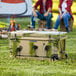 A green and black CaterGator outdoor cooler on grass with people sitting on stumps.