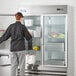 A woman standing in front of an Avantco glass door reach-in refrigerator.