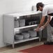 A man in a white shirt and black pants putting plates on a Regency stainless steel dish shelf in a school kitchen.