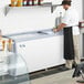 A man in a black apron serving ice cream from an Avantco ice cream dipping cabinet.